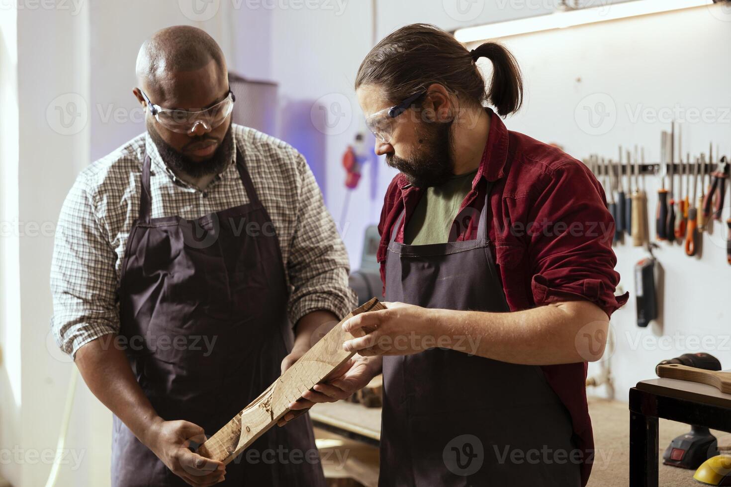 Woodworker holding timber block, brainstorming with colleague next steps in wood processing. Manufacturer and BIPOC apprentice analyzing piece of wood together, sizing it up photo