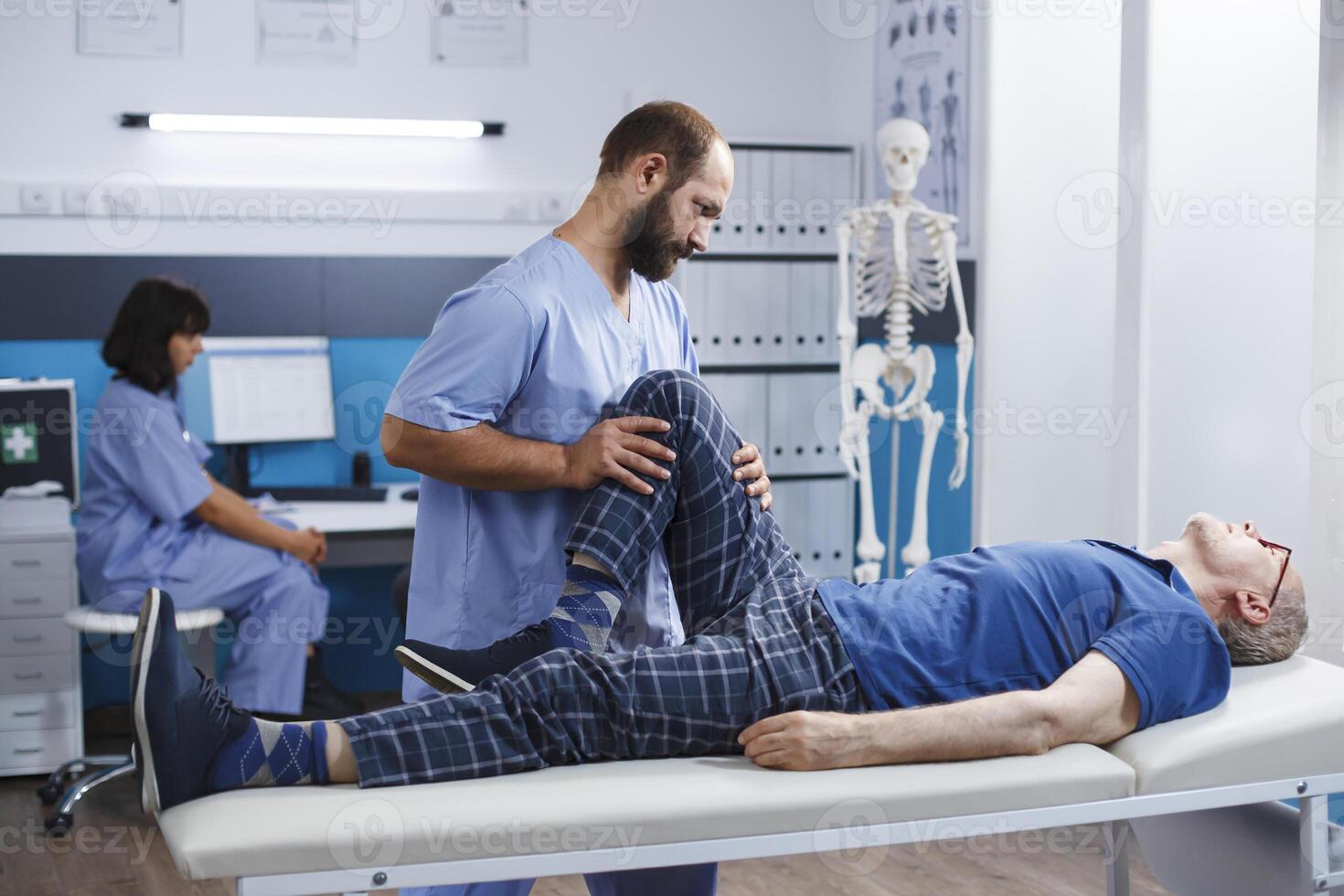 Physiotherapist assisting senior man with leg injury to recover at kinesiotherapy clinic. Nurse practitioner giving support to retired patient with knee pain and muscle pressure for recovery. photo