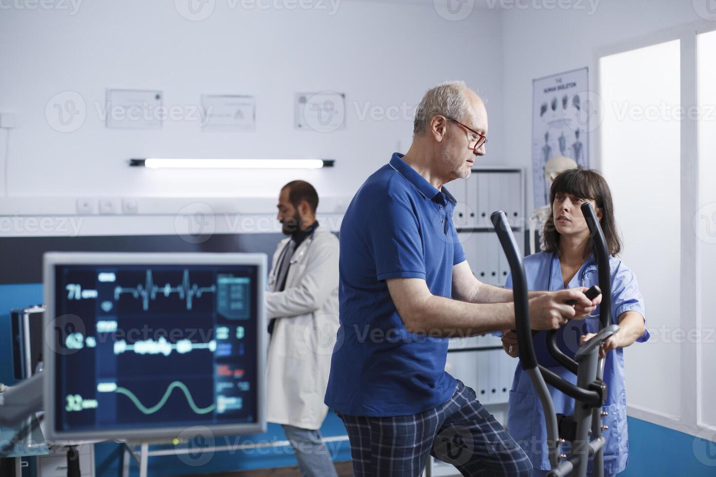 Nurse practitioner giving assistance to old man using stationary bike for physical activity and recovery. Medical assistant helping male patient with exercise bicycle for physiotherapy. photo
