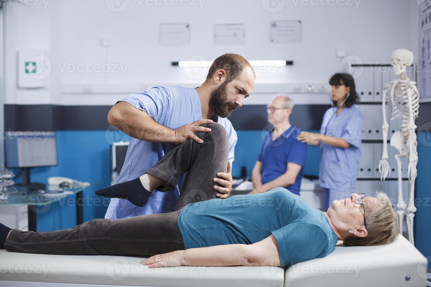 Chiropractor giving assistance to senior patient with knee injury for physical recovery. Woman doing leg exercise with help from medical assistant for osteopathic remedy and treatment. photo