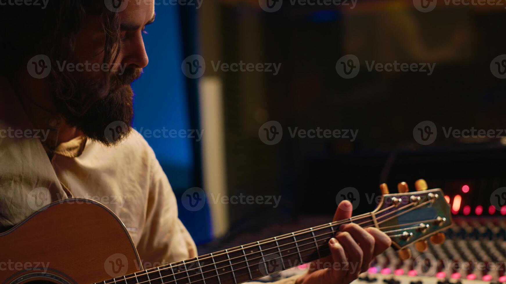 Skilled artist singing on his guitar and recording tunes for a future song, working on new album in control room at studio. Musician composer creating a new track o9n instrument. Camera A. photo