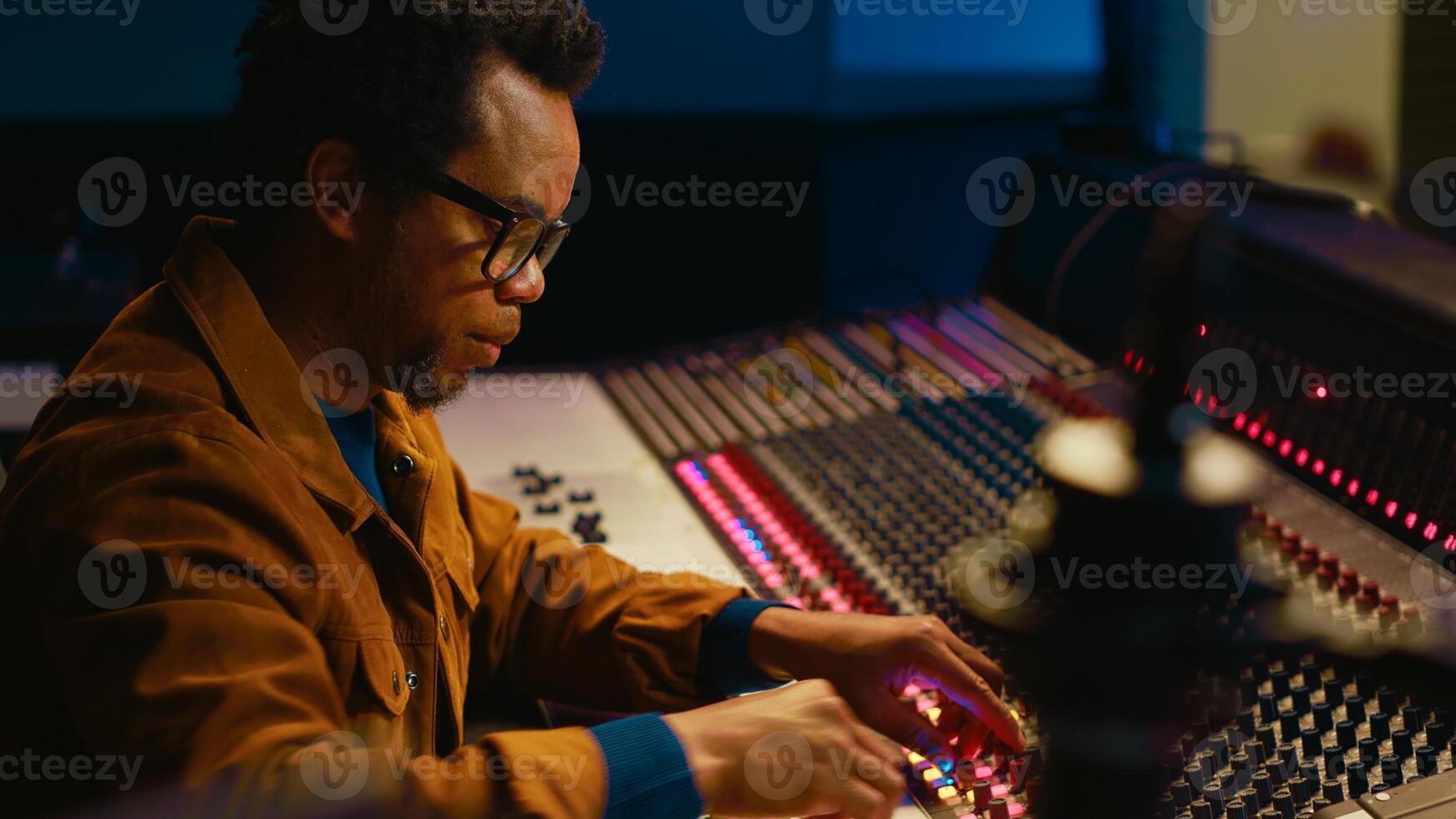 Music producer using audio mixer in professional studio, adjusting volume levels while pressing buttons and sliders on control desk. Sound designer works with digital audio software. Camera A. photo