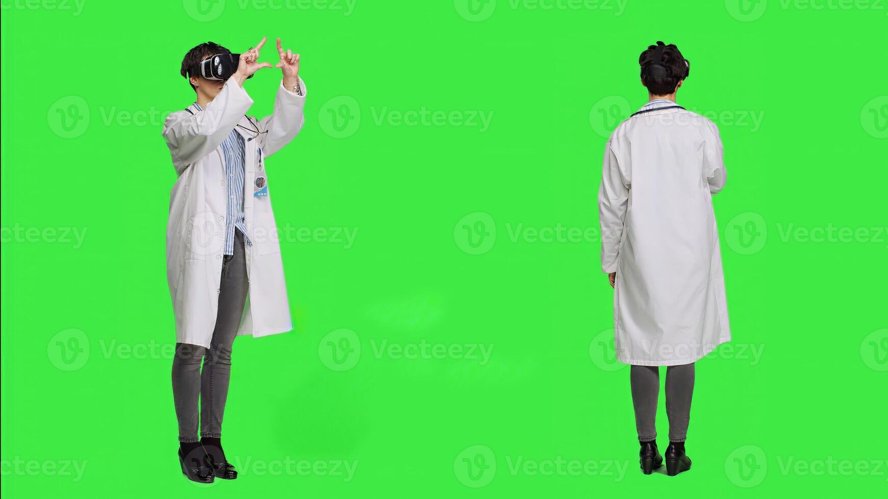 Woman medic works with 3d virtual reality headset in studio, standing against greenscreen backdrop. General practitioner uses vr glasses with interactive vision tool, futuristic exam. Camera A. photo