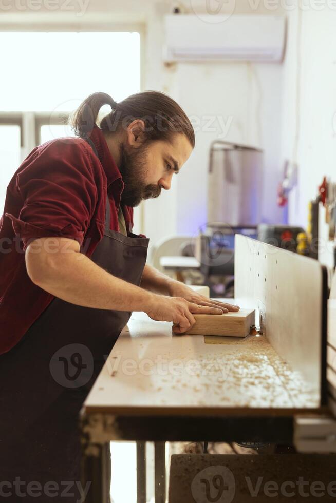 Craftsperson putting lumber block though spindle moulder, doing furniture assembling. Joiner in carpentry studio using heavy machinery to perform various manufacturing tasks, enjoying diy hobby photo