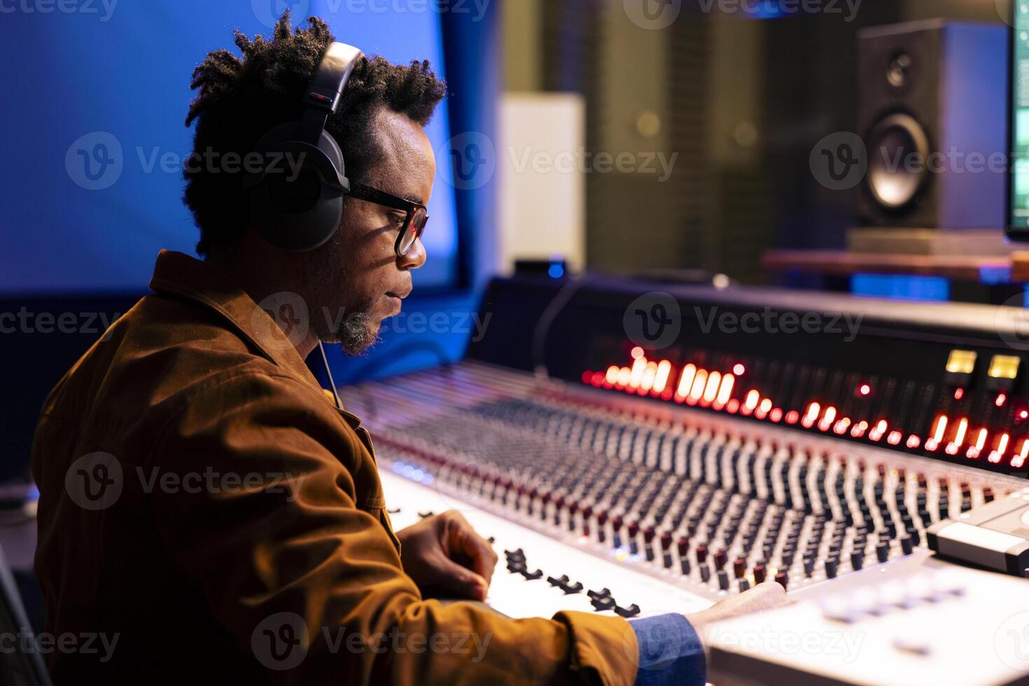 African american audio expert editing tracks in professional recording studio, mixing and mastering music in control room with technical gear. Sound engineer producing new tracks for an album. photo