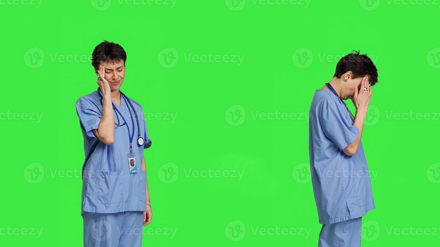 Unwell nurse suffering from a headache against greenscreen backdrop, wearing scrubs and feeling overworked at hospital. Medical assistant having a painful migraine, stress and burnout. Camera B. photo