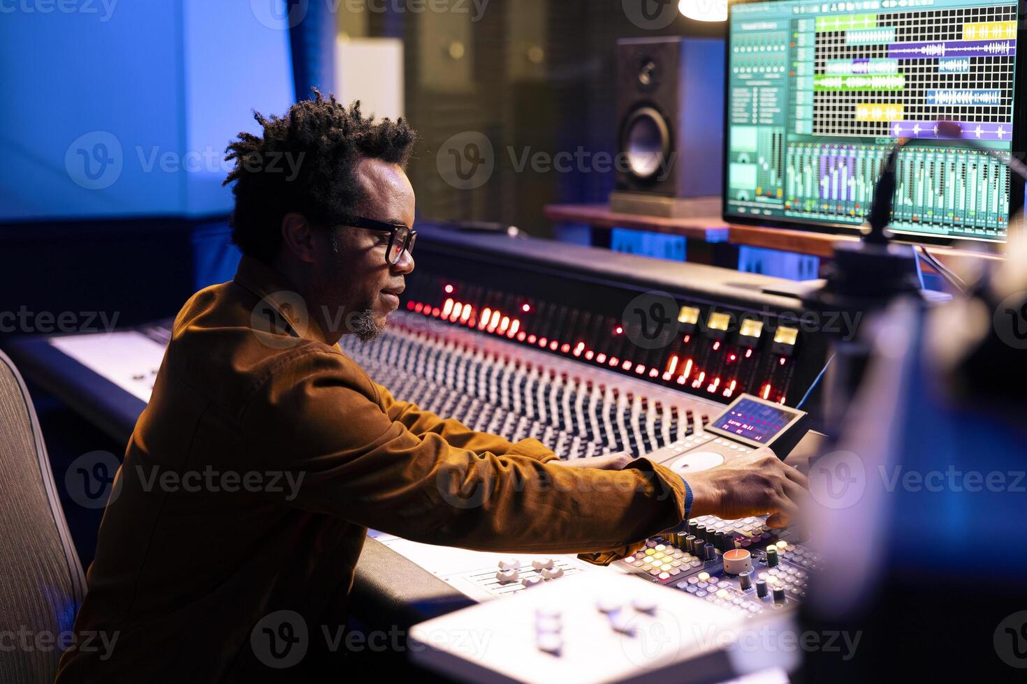 African american music producer composing tracks in control room, editing songs and adjusting volume settings with dashboard knobs. Audio engineer pressing faders and buttons. photo