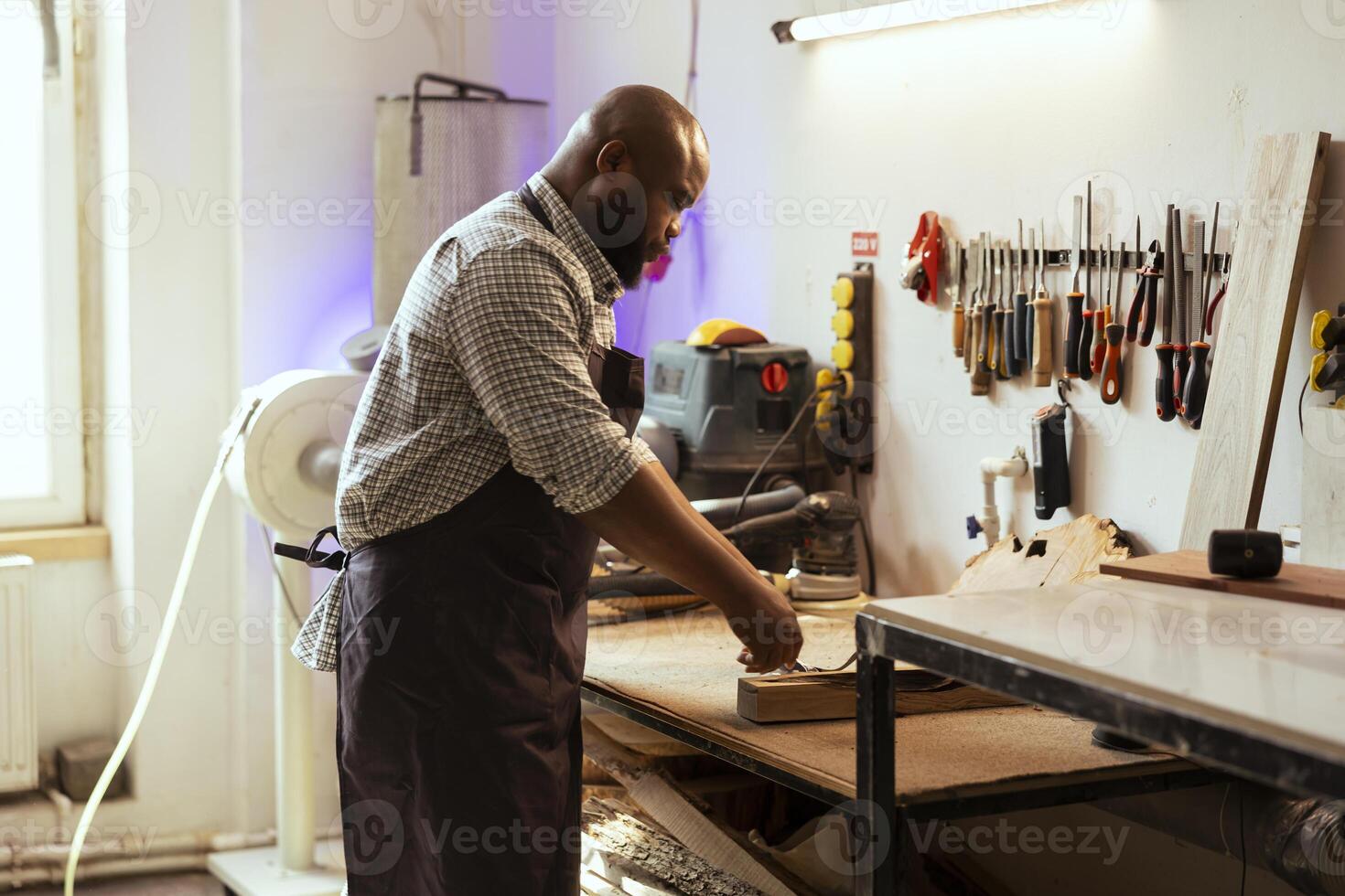 Craftsperson at workbench selecting high quality wood materials for commissioned project. African american woodworking professional doing quality assurance on timber piece photo