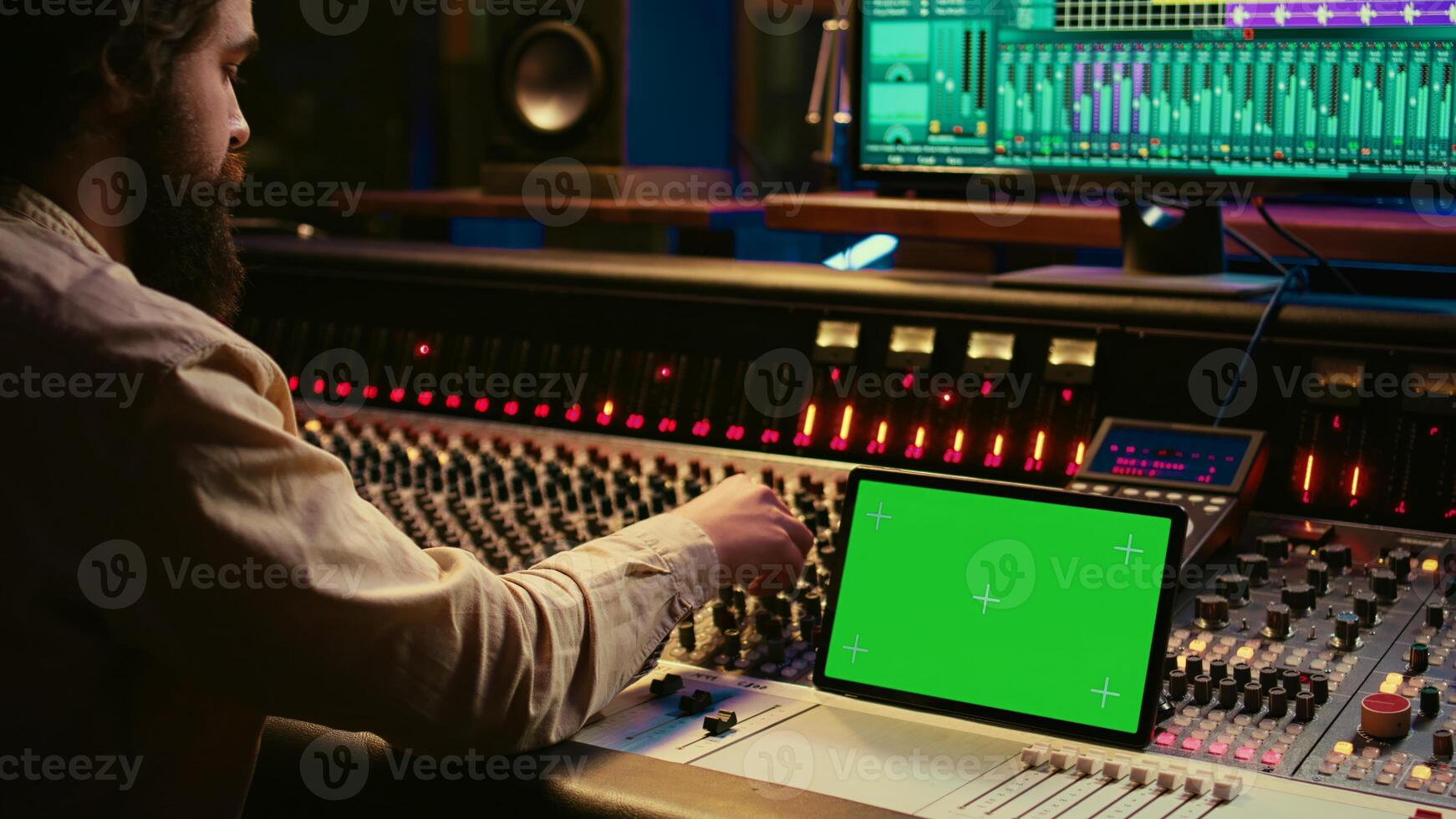 Audio expert mixing and mastering tunes on editing software next to greenscreen tablet, producing and recording tracks by pushing buttons and faders. Sound engineer in control room. Camera B. photo