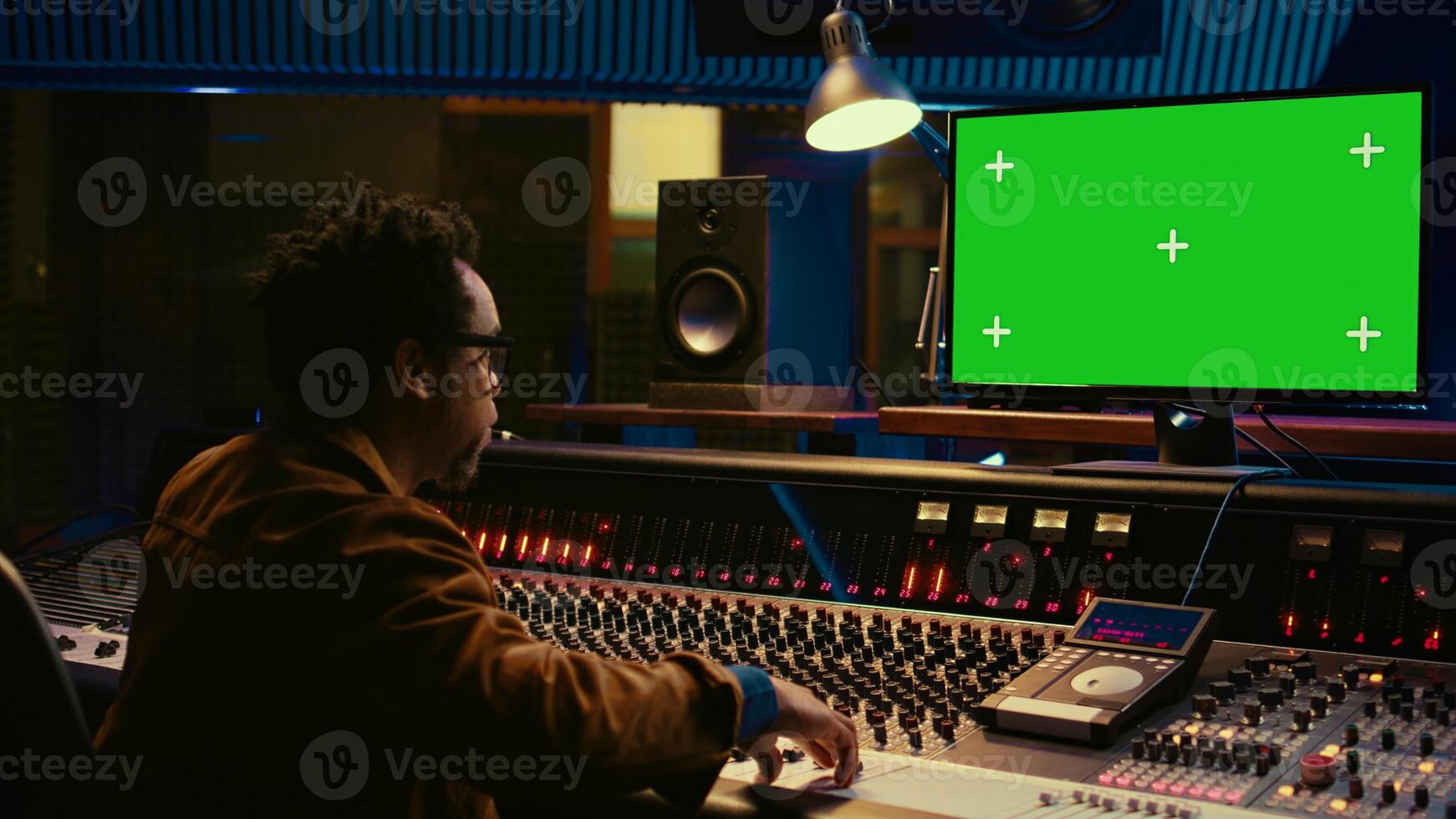 African american sound designer looks at greenscreen to record and edit tunes, uses mixing console to create new songs. Skilled technician works on processing and track recording. Camera B. photo