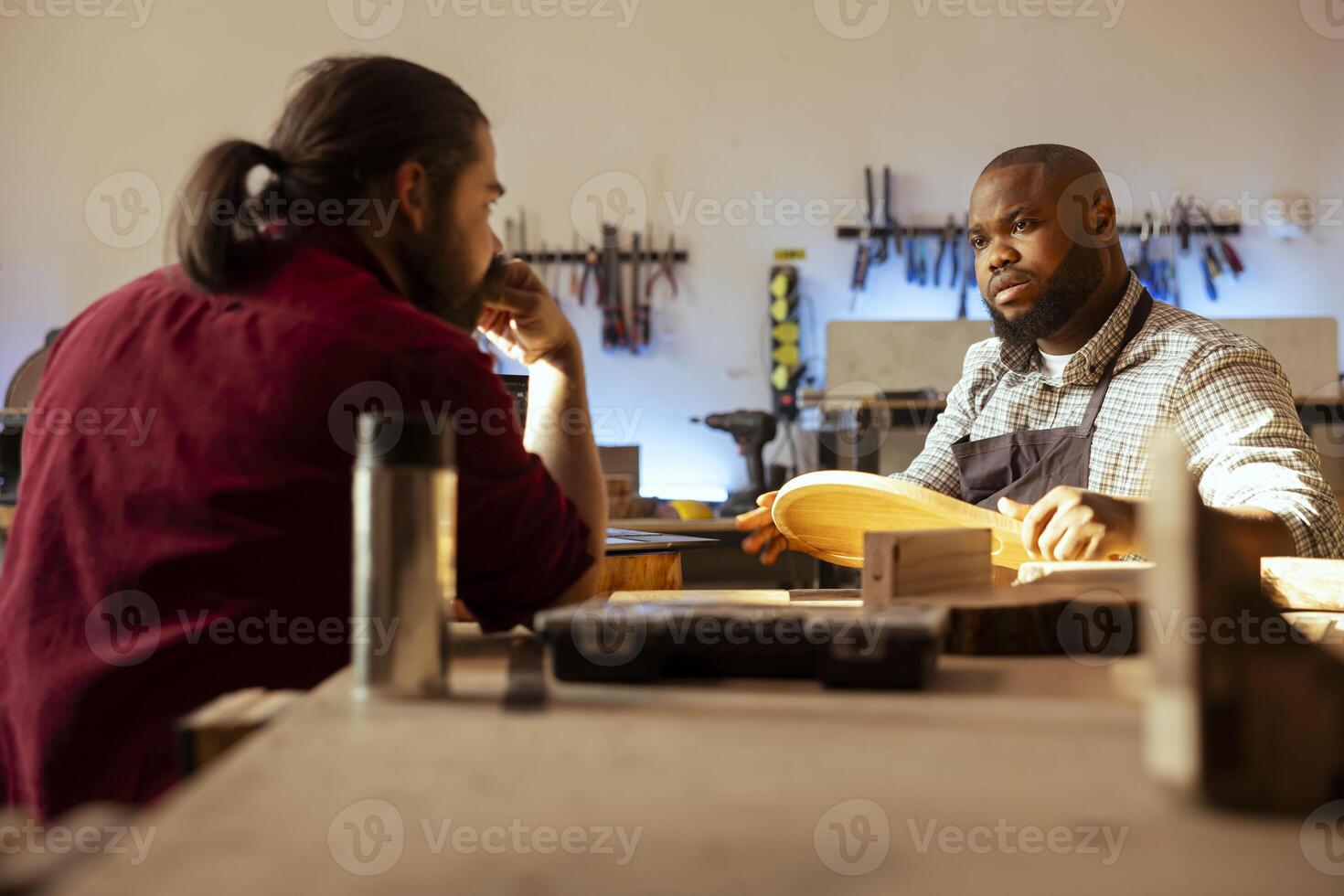 Manufacturer and apprentice discussing in studio to select best wood materials for project. Cabinetmaker and colleague talking in joinery, doing quality assurance on lumber piece photo