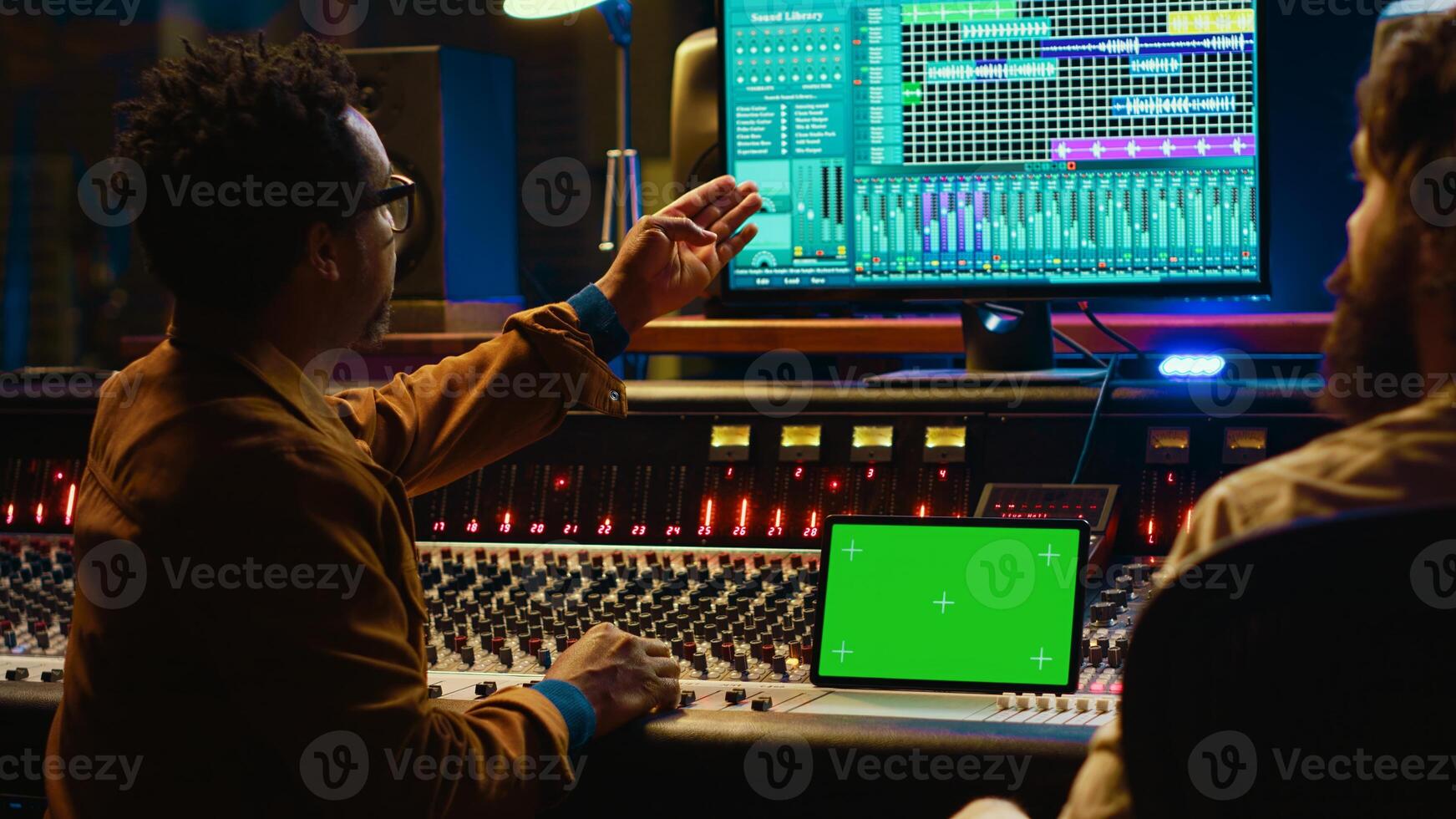 Professional engineer and musician mixing tracks next to isolated display on tablet, editing audio after recording session to produce a hit song. Artist collaborates with sound designer. Camera A. photo