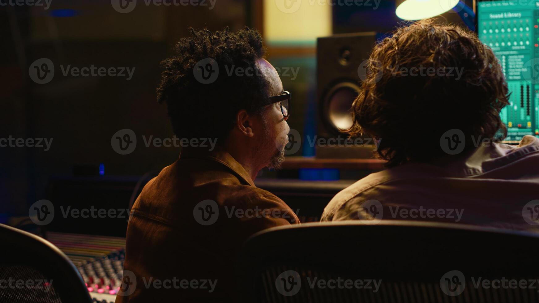 Musician and audio technician collaborating on mixing tracks to create a successful hit in professional studio. Team of experts listening to recordings and adding effects in post production. Camera A. photo