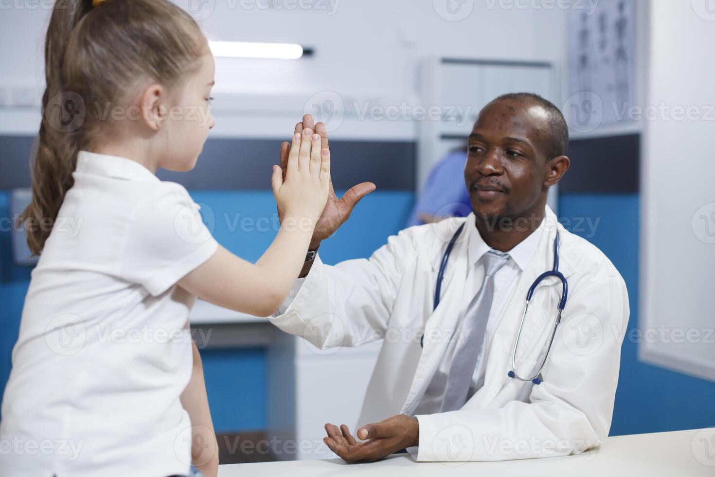 africano americano médico dando alto cinco a un joven niño durante médico cita en hospital oficina. negro hombre con un laboratorio Saco explicando enfermedad síntomas que se discute cuidado de la salud tratamiento. foto