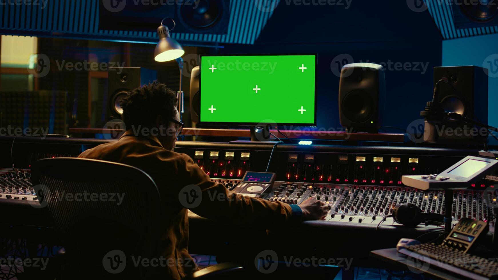 African american music producer working with greenscreen on pc, using mixing console to do mix and master in control room. Audio technician recording tracks with knobs and switchers. Camera B. photo