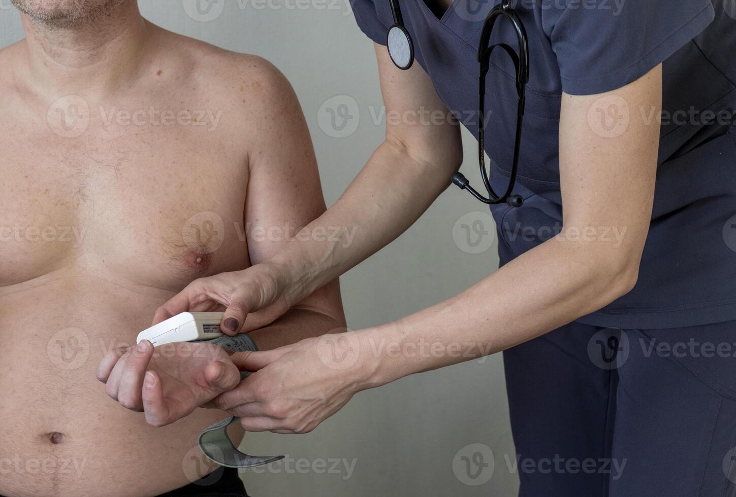 Shot of the female doctor in uniform against the white wall examining mid age male patient, helping him to check blood pressure. Healthcare photo