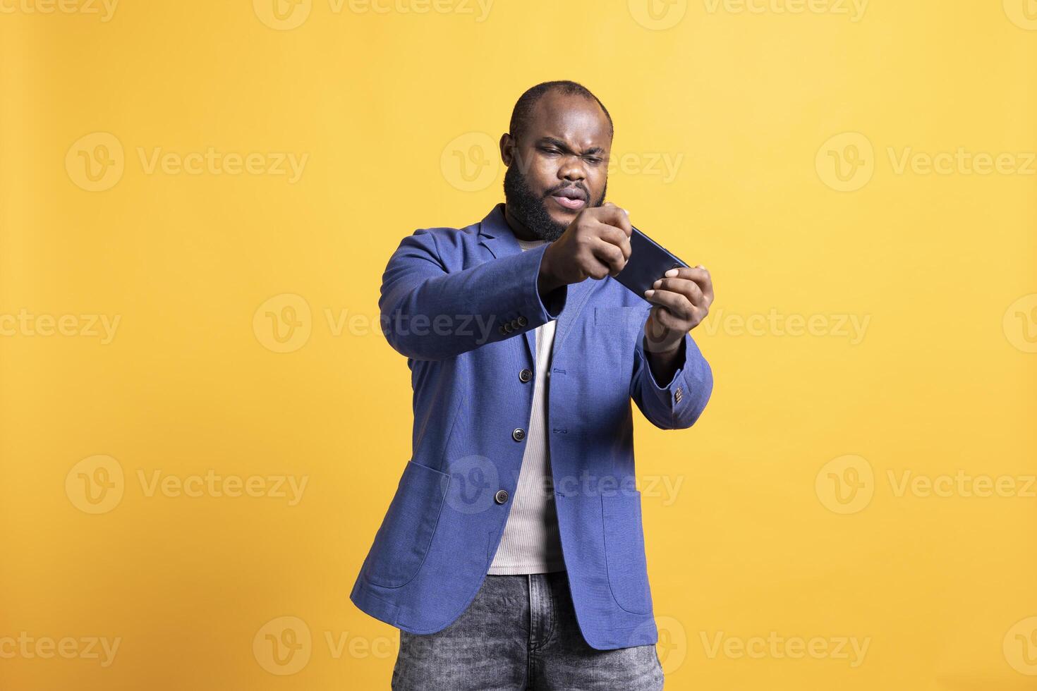 BIPOC man playing intense games on cellphone, enjoying entertainment. African american gamer enjoying game on mobile phone, having fun, isolated over yellow studio background photo