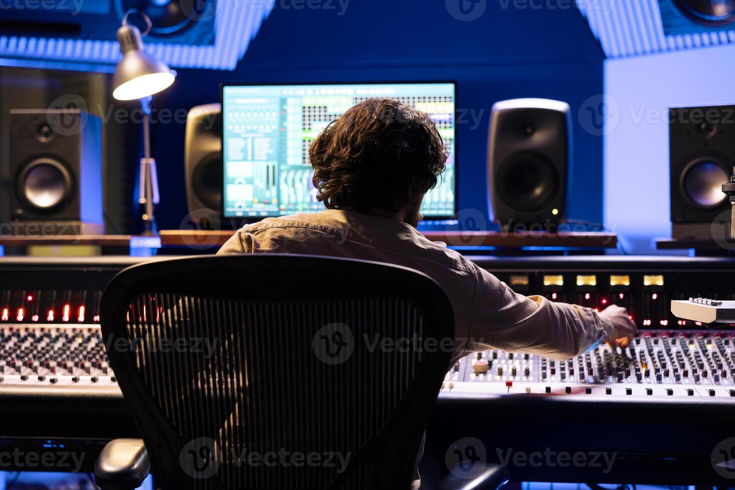 Skilled sound designer working on digital audio software app, editing tracks with mixing console and control panel board. Male engineer producing music with faders and buttons in studio. photo