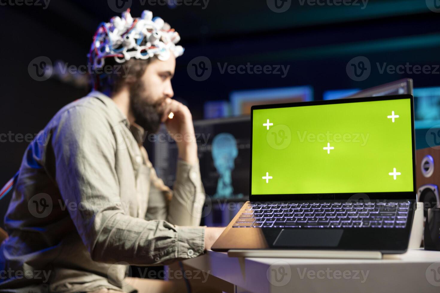 Man with EEG headset on writing code to transfer mind into virtual world, isolated screen laptop on desk Transhumanist using neuroscientific tech and chroma key notebook to gain superintelligence photo