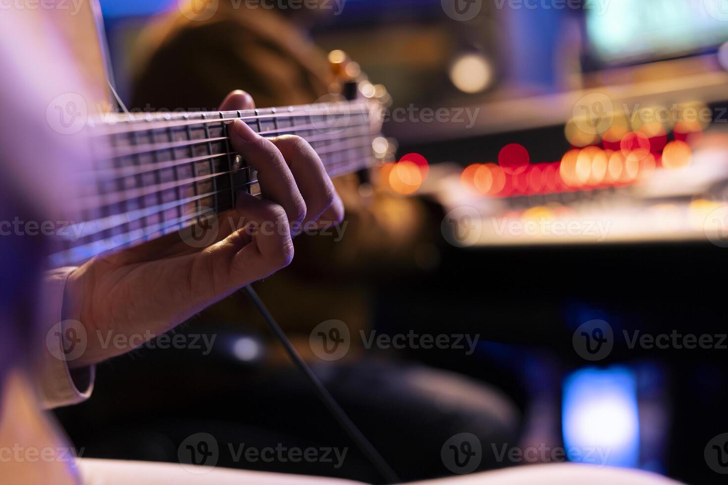 Talented singer playing new accords on electro acoustic guitar in music studio, recording new songs with audio engineer in control room. Male musician producing tracks on instrument. Close up. photo