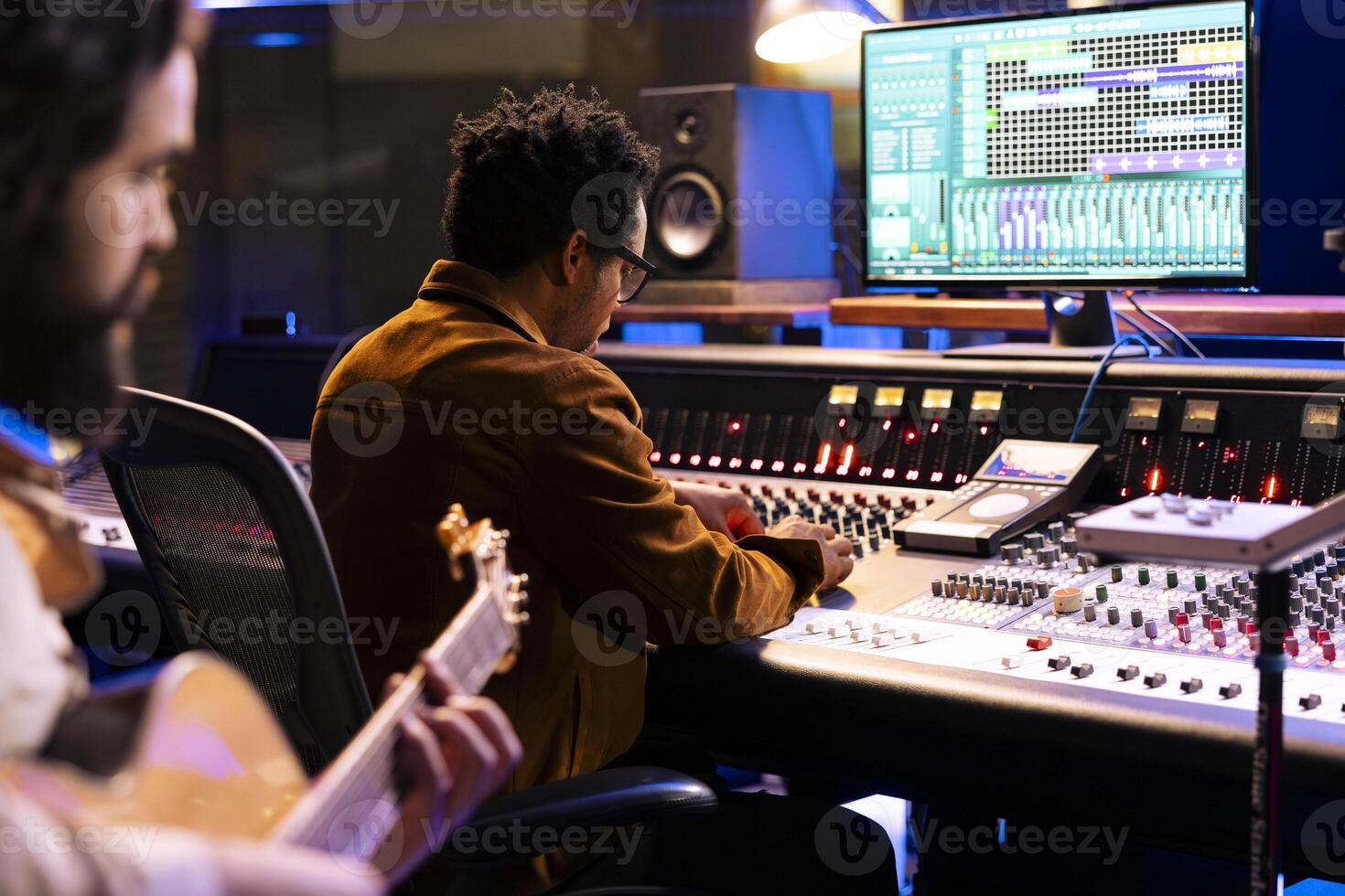 Skilled songwriter artist recording a song with electro acoustic guitar tunes, making music for his pop rock album. Musician singing tracks on instrument in control room, works with audio expert. photo