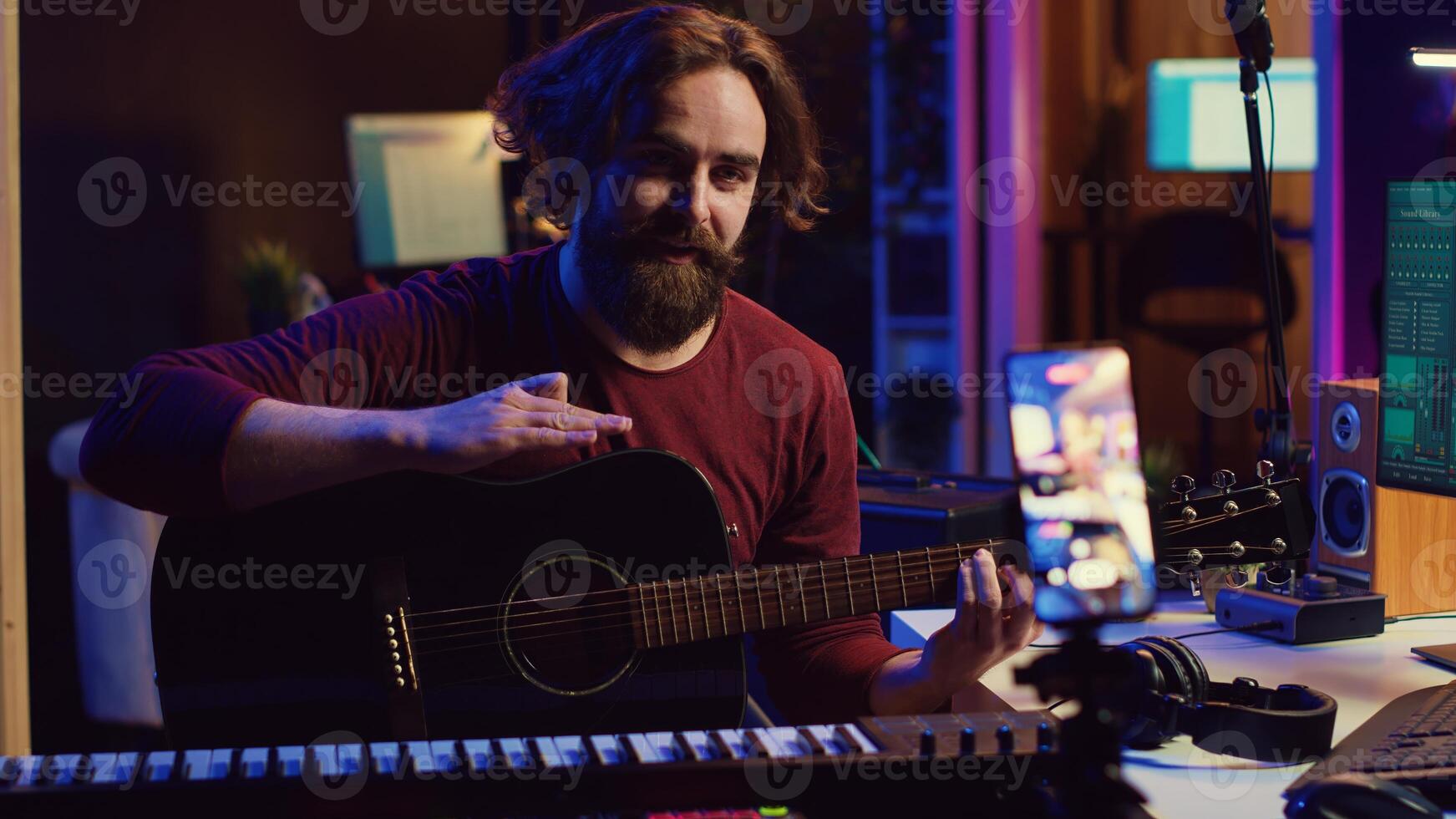 Artist recording himself at home singing and playing acoustic guitar, filming vlog about learning to sing popular songs. Musical performer teaching online lessons on smartphone. Camera A. photo