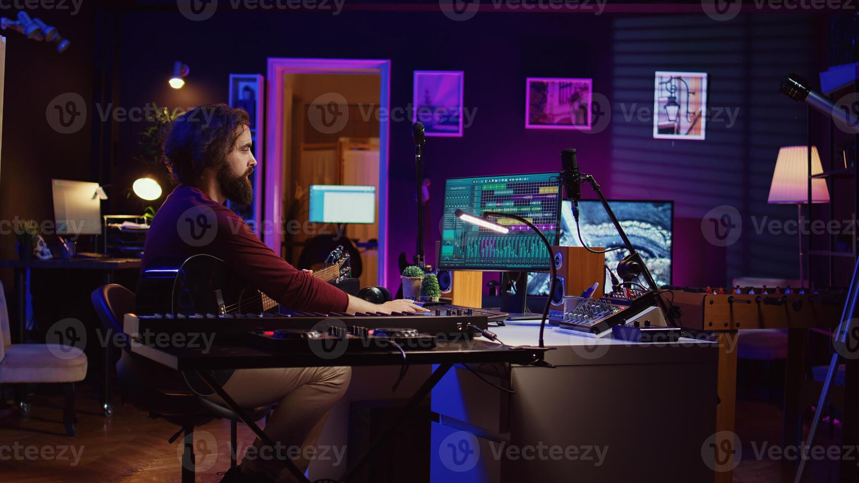 Music producer operating with electronic setup of home studio, recording acoustic guitar sounds. Artist navigating signal processing activity, utilizing digital audio workstation at desk. Camera B. photo