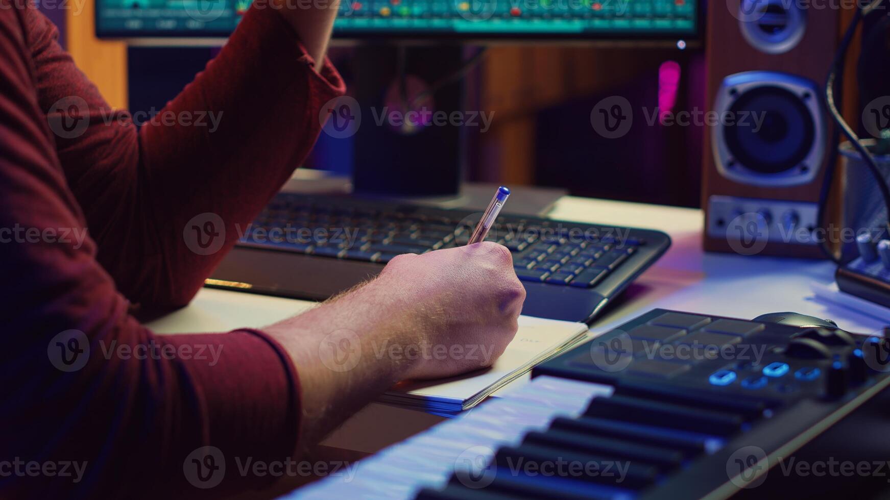 Composer developing an original track In his home studio, writing down lyrics and harmonic notes before recording the song melody. Musician using DAW computer apps for creating music. Camera A. photo