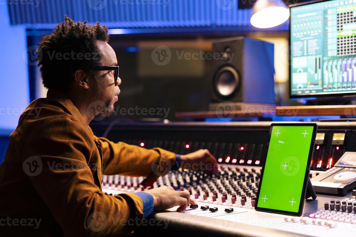 African american music producer recording and editing tracks in studio, operates panel board next to mockup on device. Sound designer mixing and mastering tunes on audio console, stereo gear. photo