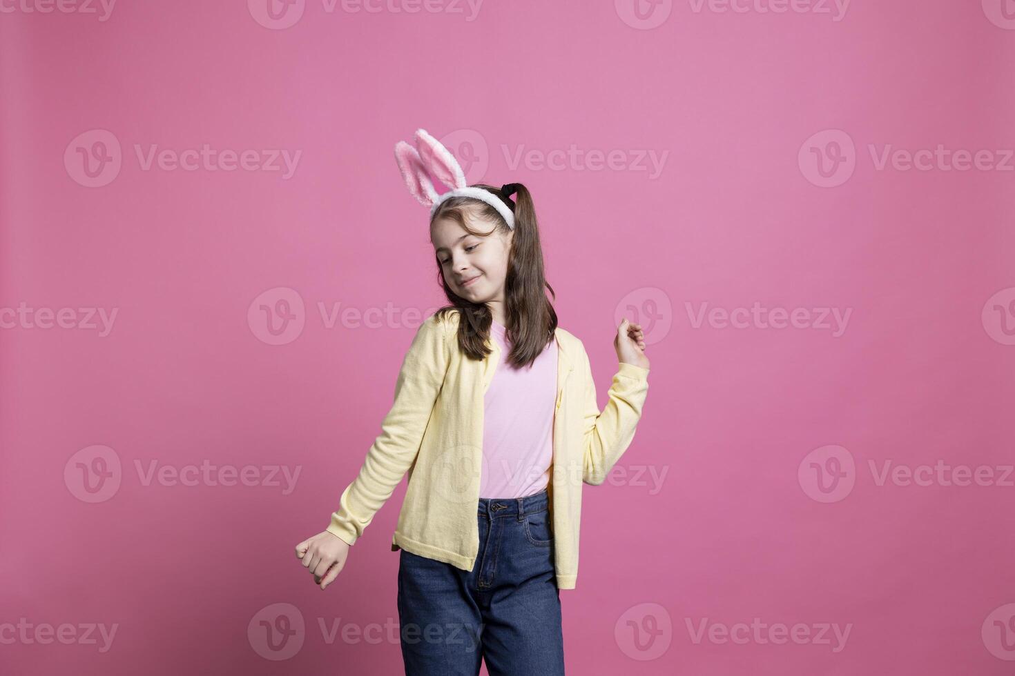 Happy cheery junior dancing around in the studio with fluffy bunny ears, preparing to celebrate easter sunday festivity. Young joyful toddler feeling carefree and confident with dance moves. photo