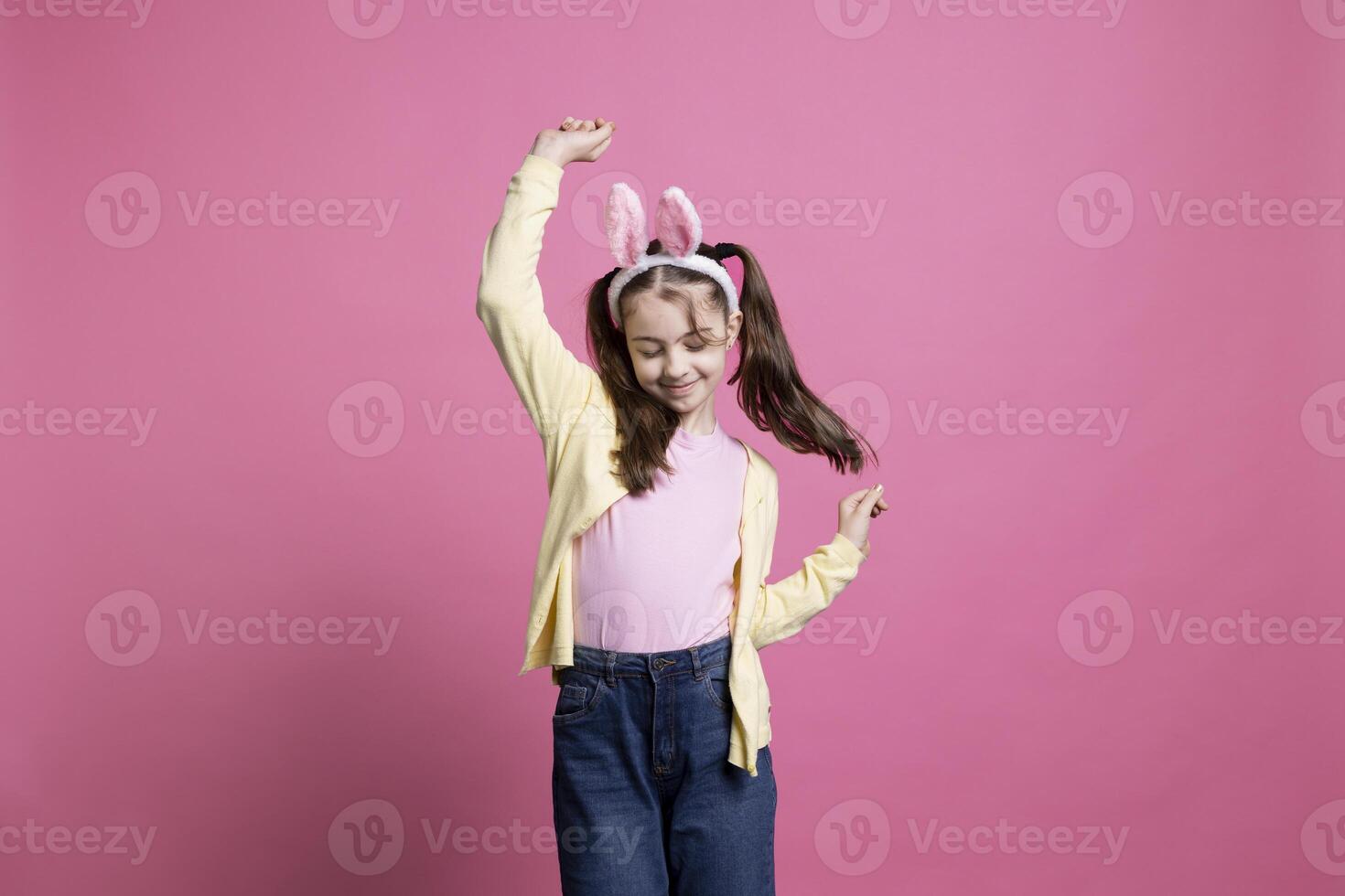 Energetic and positive kid dancing in studio while wearing bunny ears in excitement of Easter Sunday celebrations. Pleased carefree youngster who displays comfort in her dance skills. photo