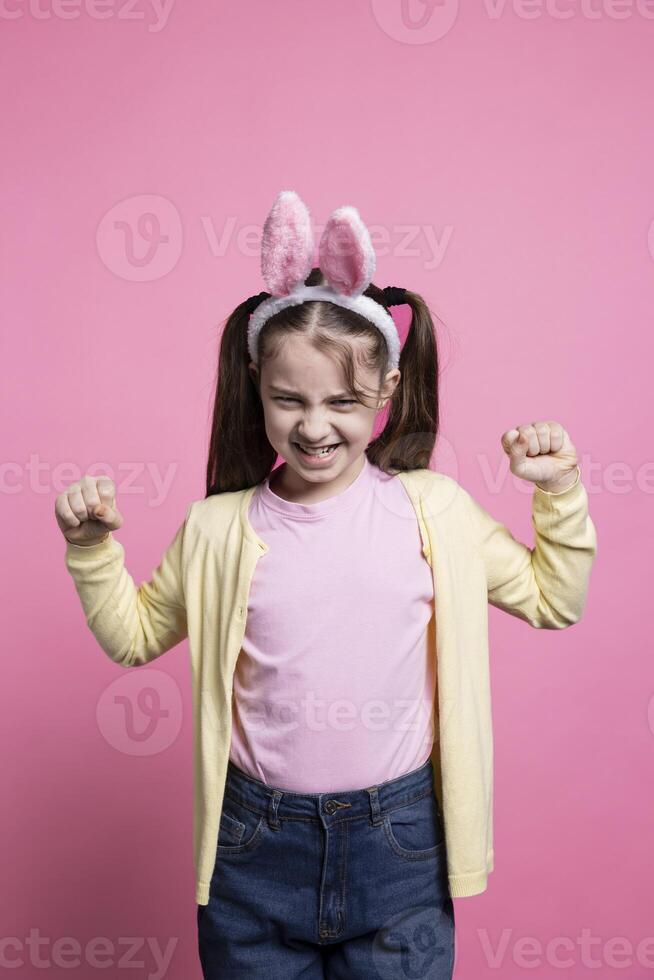 Angry irritated young girl expressing her disappointment in studio, wearing bunny ears buy feeling displeased about something. Little toddler shows her disapproval, negative emotions. photo