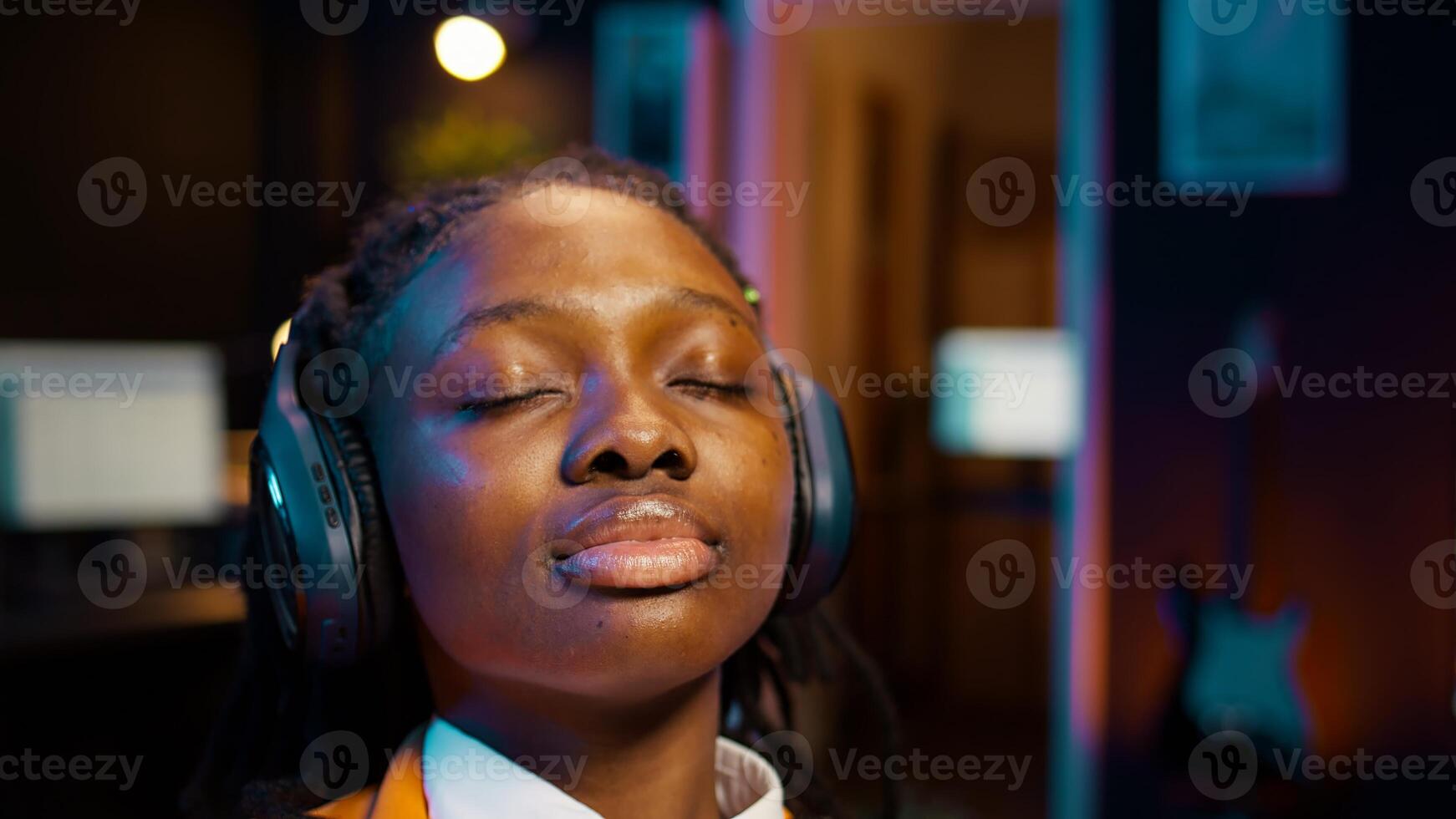 College student sitting laid back after working on class project, relaxing with ambience music on headphones at home desk. African american girl chilling with modern tunes on headset. Camera B. photo