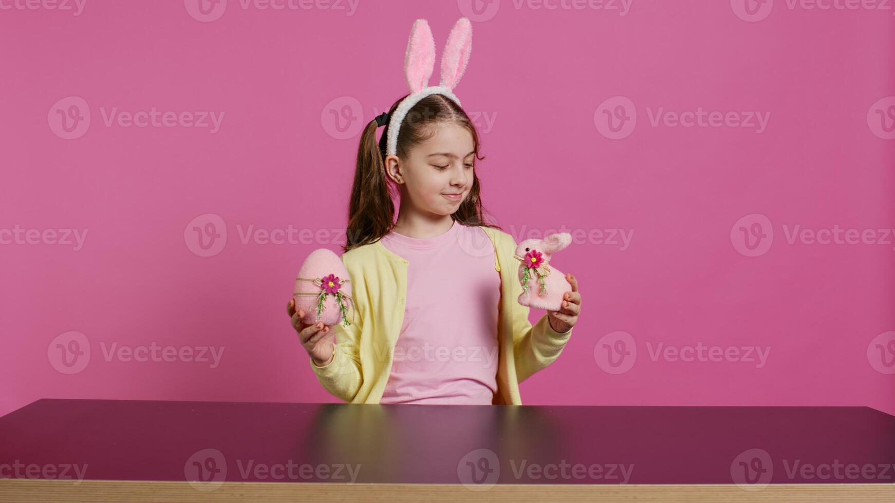 Small cheerful girl showing colorful decorated ornaments on camera, creating handcrafted festive arrangements. Young child feeling excited about easter sunday, holds rabbit and egg. Camera B. photo