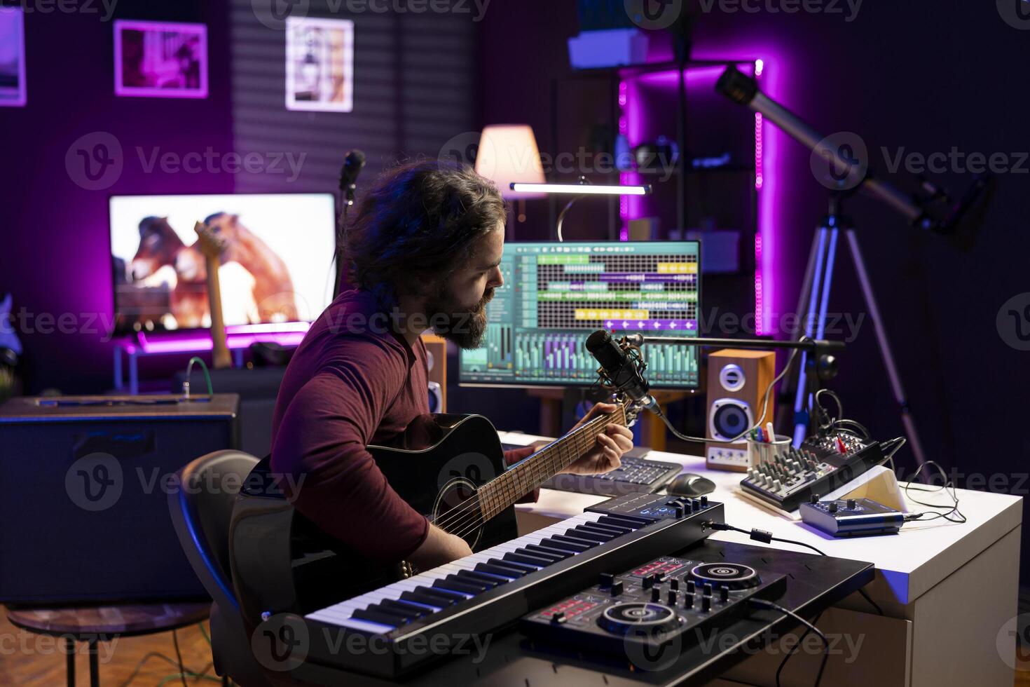 Musical artist recording his acoustic guitar accords in home studio, creating a beautiful song by singing lyrics on microphone. Producer uses mixing console and daw software to compose tunes. photo