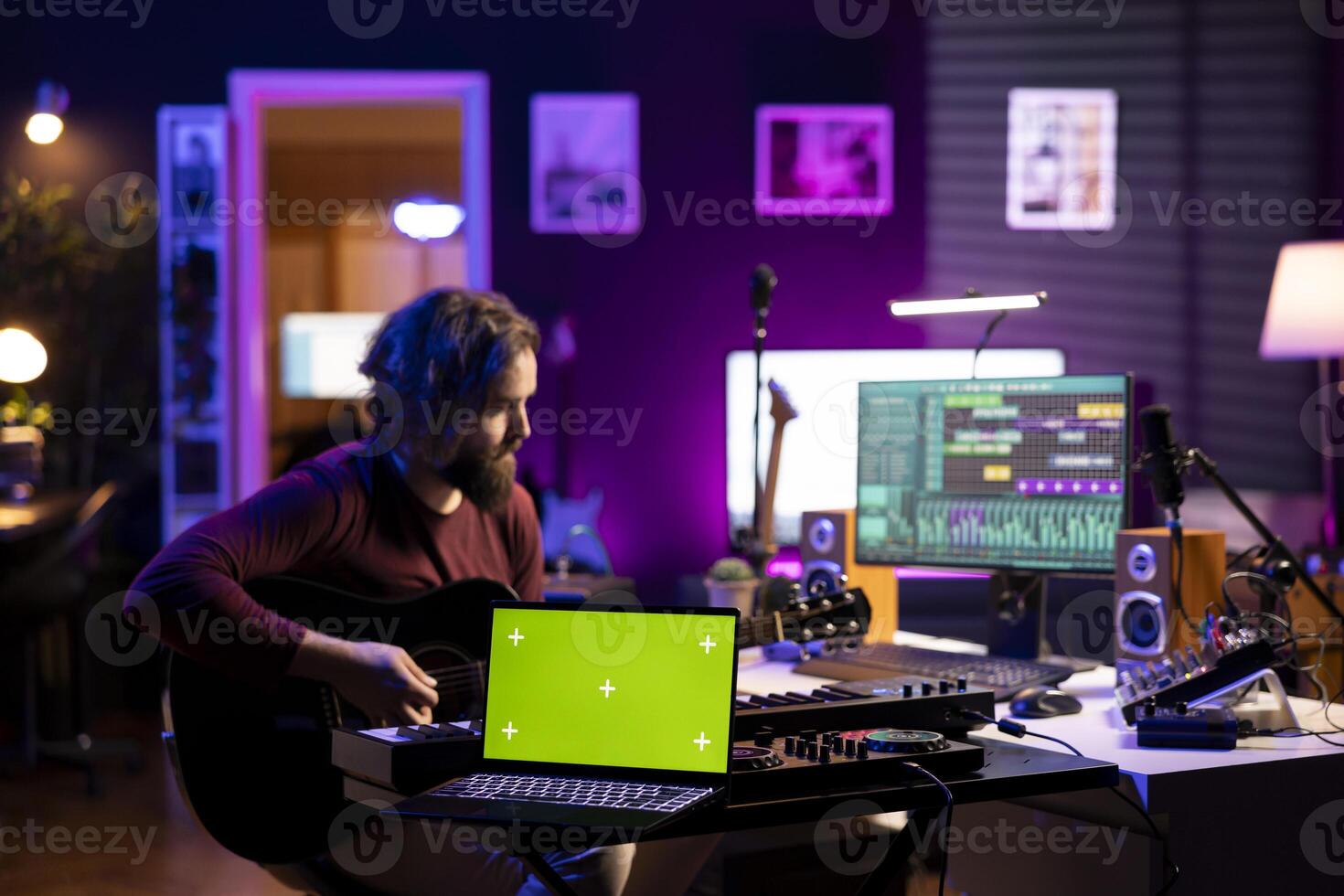 Musical performer playing acoustic guitar next to greenscreen layout on laptop, recording tunes using mixing console and daw software. Artist trying new accords on instrument, music industry. photo