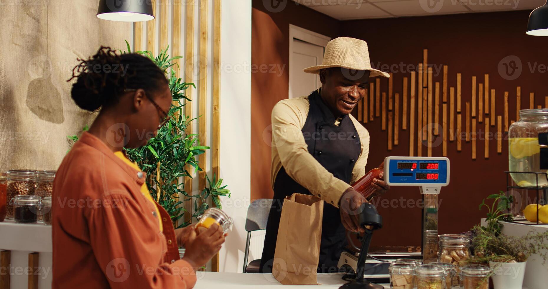 African american woman bringing natural products at checkout, talking to vendor about healthy eating while he scans goods. Local farmer selling his homegrown veggies and homemade items. Camera 2. photo