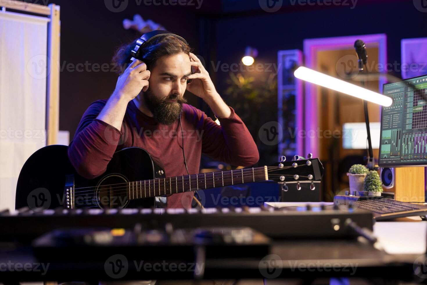 Sound composer operating with electronic setup in home studio, recording and playing acoustic guitar tunes. Musician working with signal processing techniques and audio plug ins at desk. photo