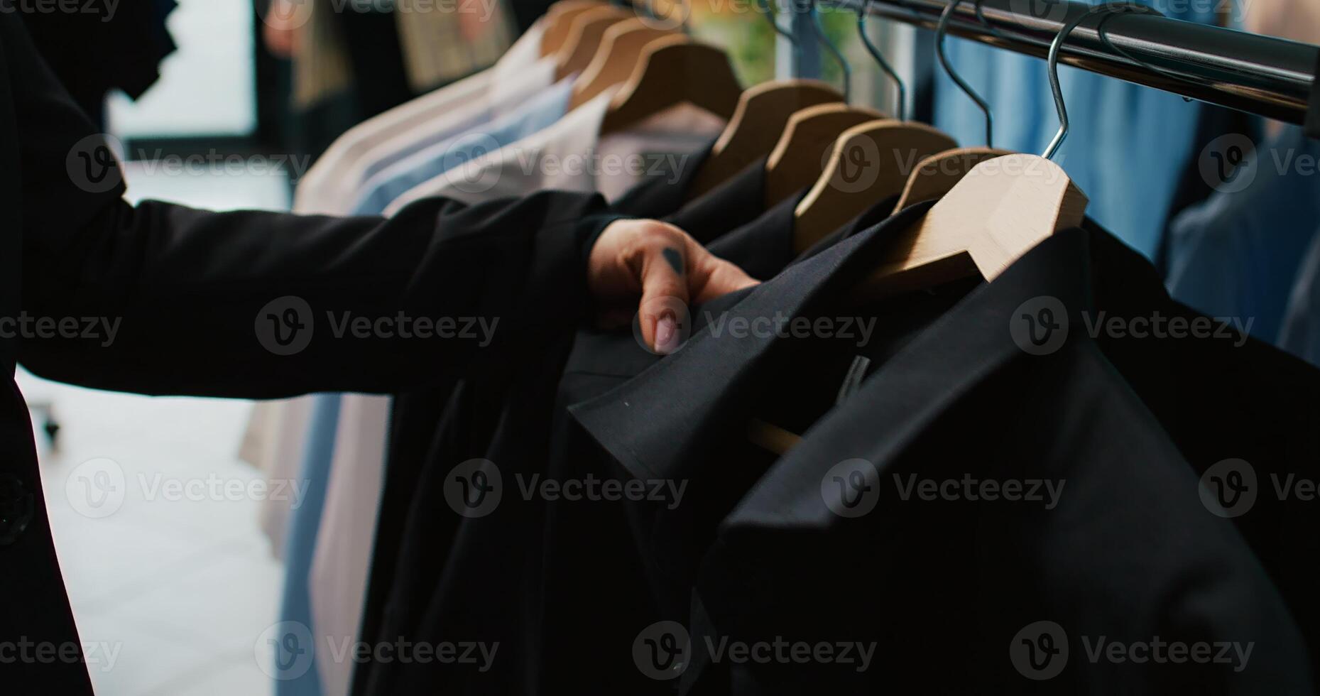 Classy woman examining all colorful shirts on display at clothing store, shopping for trendy brands to expand wardrobe. Customer looking at fashion items stored on hangers. Close up. Camera B. photo