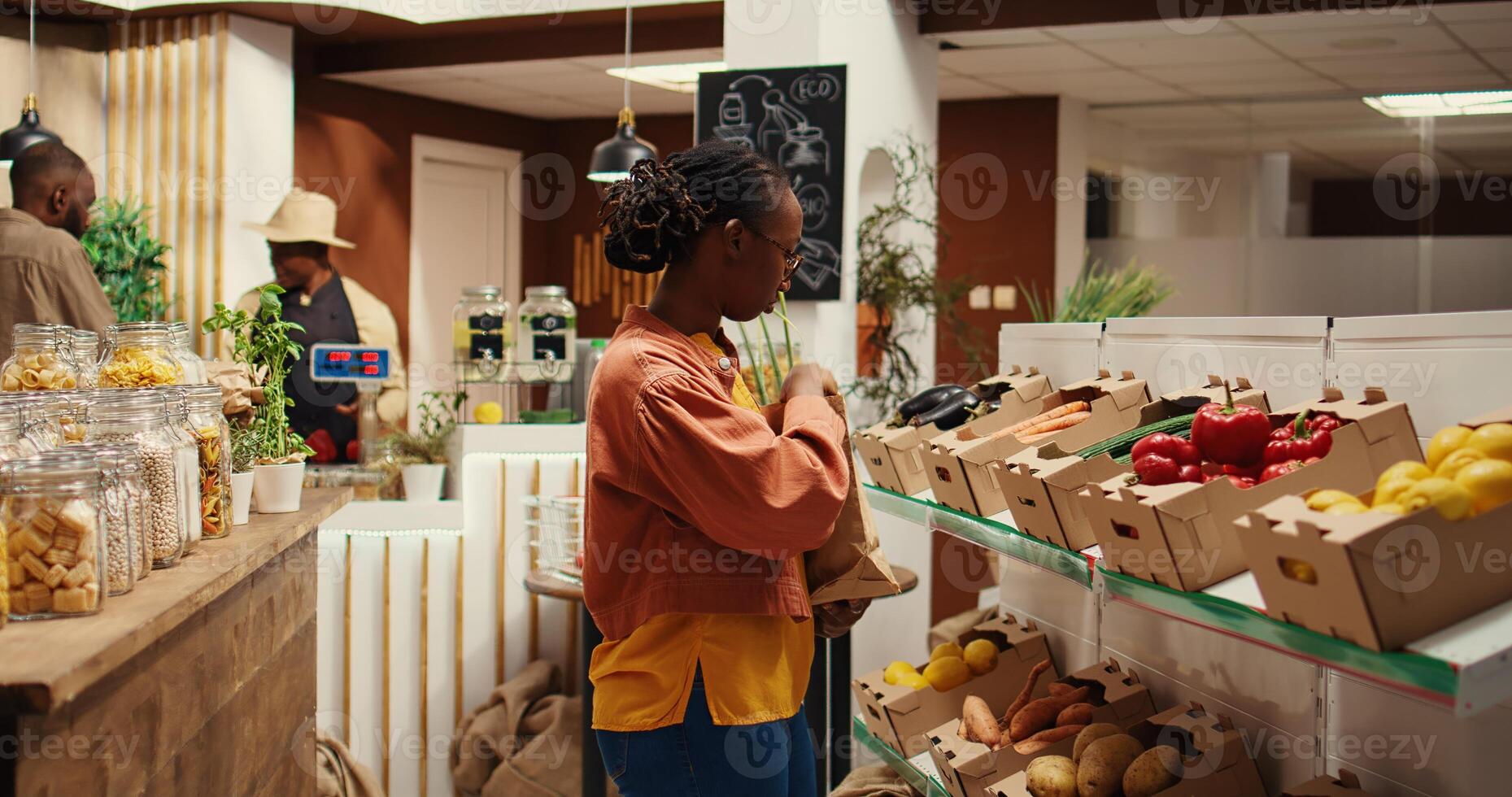 Vegan person searching for freshly harvested vegetables from crates, shopping for natural groceries at local zero waste eco store. African american client looking at organic food items. Camera 2. photo