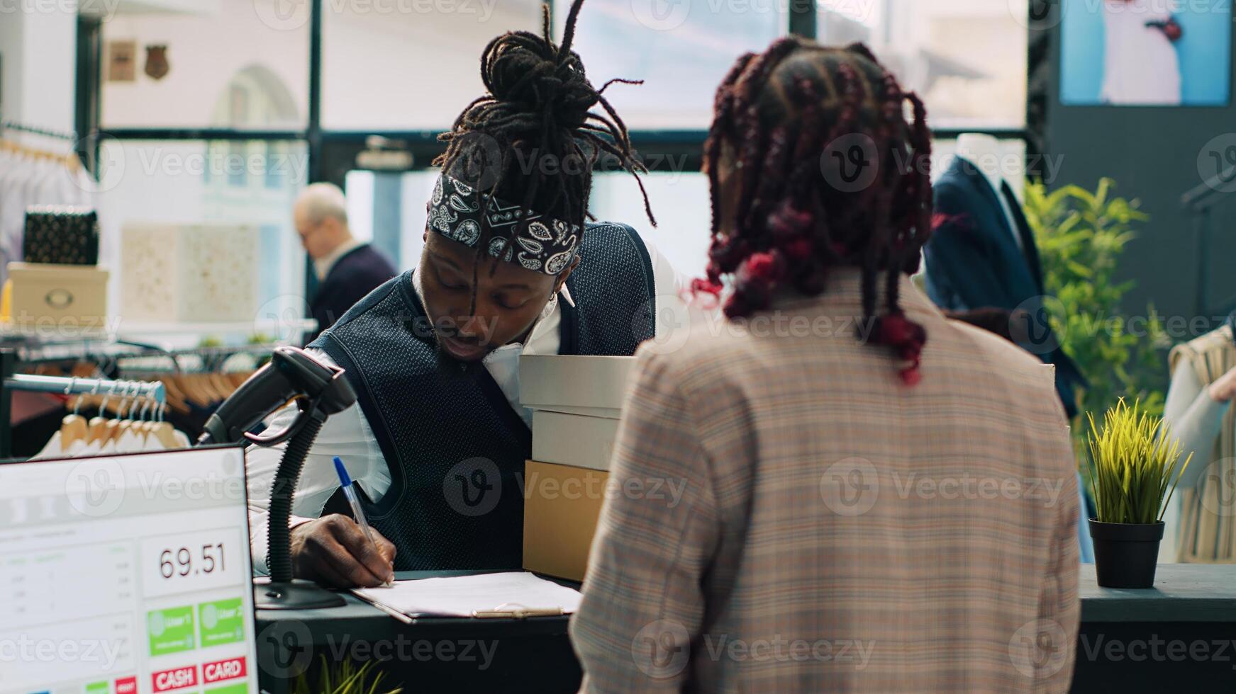 African american deliveryman receiving requested clothes packed in boxes, arriving at fashion showroom to pick up order and sign papers. Woman employee preparing items at cash register. Camera A. photo