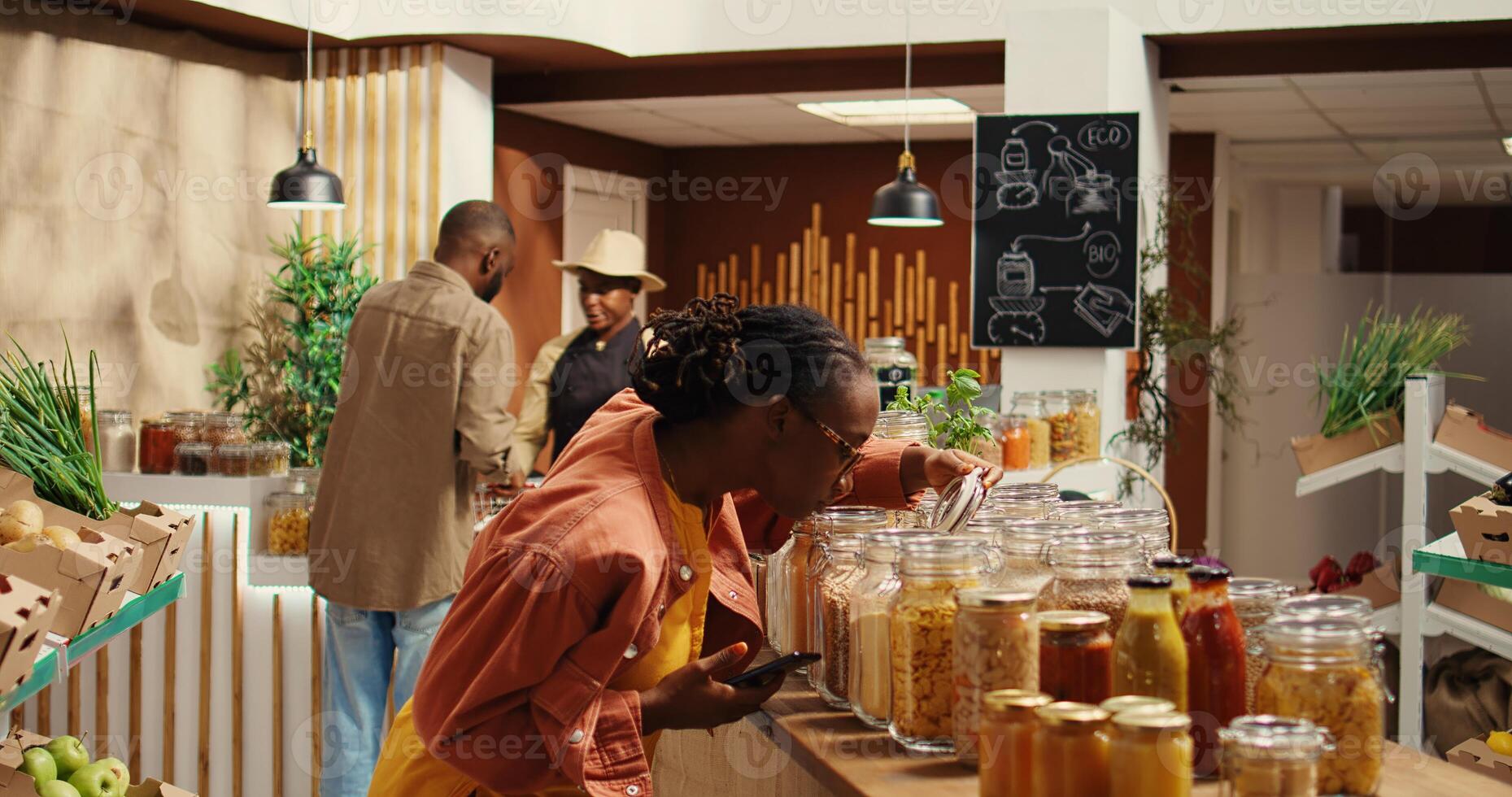 Customer checking shopping list on phone before choosing products, trying to buy organic locally grown food for low carbon footprint. African american woman looking at checklist notes. Camera 2. photo