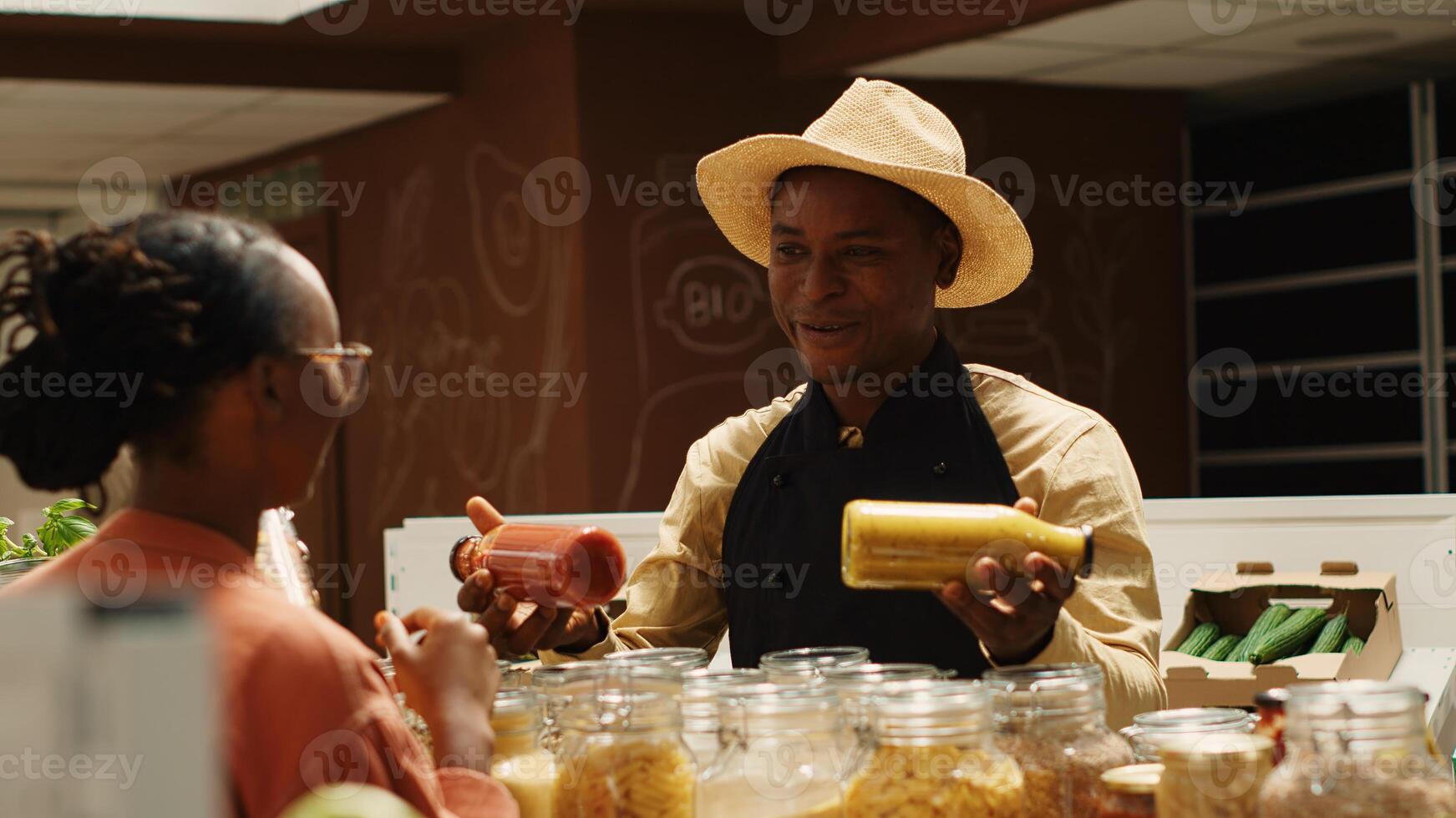 Merchant presenting additives free homemade sauces for tasty meals, recommending ethically sourced pantry supplies and pasta. Seller promoting his organic bulk products in glass jars. Camera 1. photo