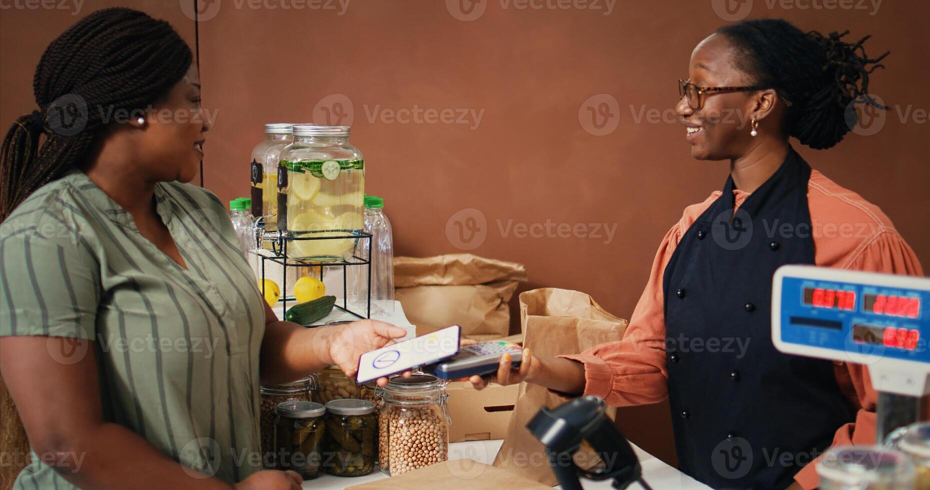 Shopper paying with smartphone at pos terminal, buying freshly harvested produce and bio pantry essentials. African american customer using nfc payment for fruits and veggies. Handheld shot. photo