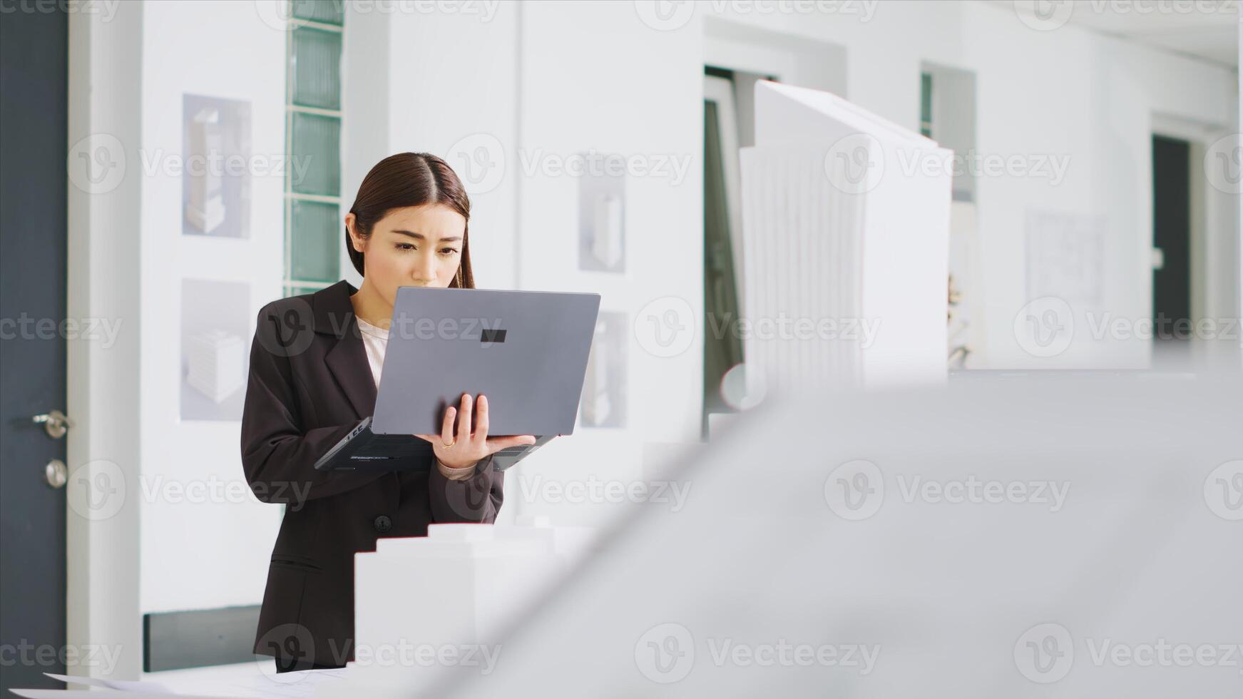 Engineer uses laptop to identify scaling features while observing 3D printed model of a building. Real estate agency worker reviewing construction scheme for new development project. photo