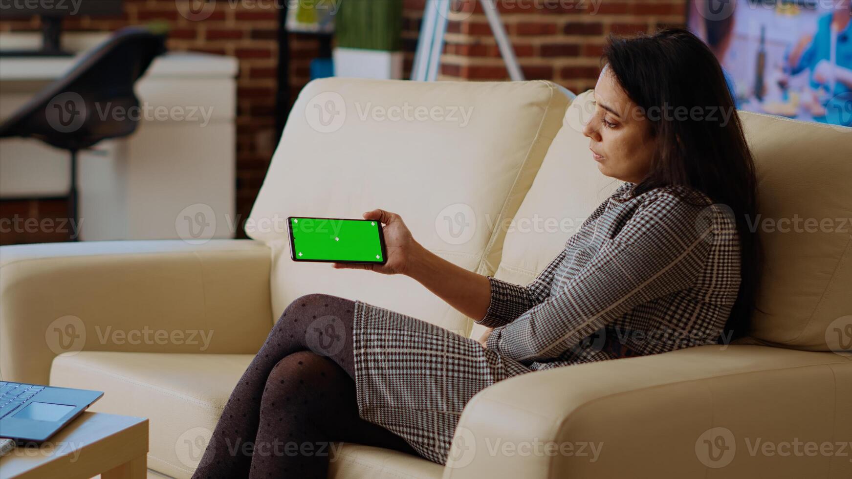 Relaxed stay at home worker enjoying herself, watching videos on chroma key smartphone. Chilled out woman sitting on couch looking at internet clips on isolated screen phone photo