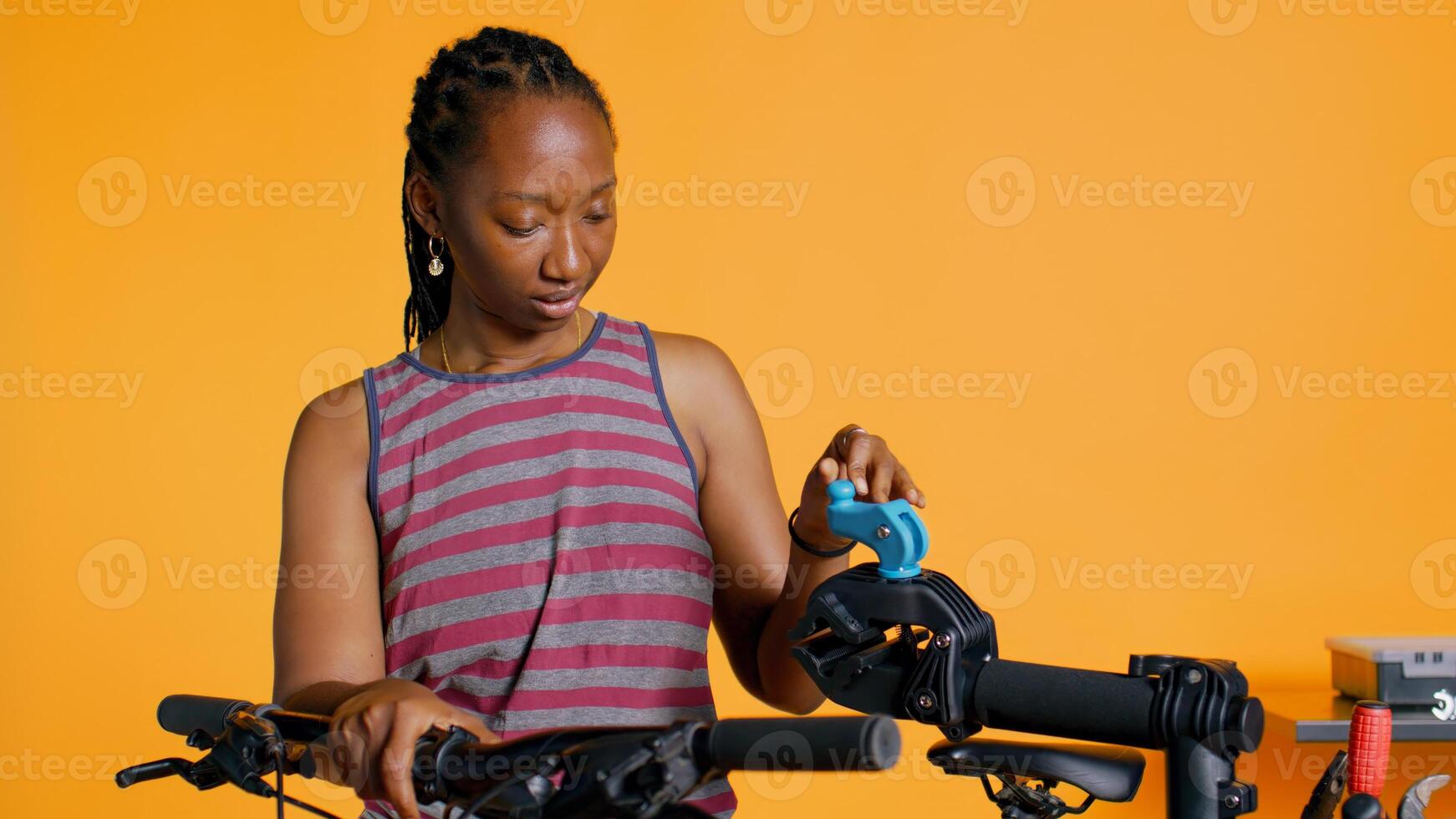African american woman setting up bike repair stand, using it to adjust derailleur, fixing broken wheels, studio background. Professional placing bicycle on workstand to do checkup on it, camera B photo