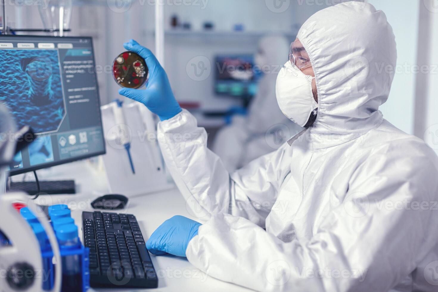 medicina investigador trabajos en SARS-CoV-2 en petri plato vestido en mono. doctores analizando vacuna evolución utilizando alto tecnología investigando diagnóstico en contra covid19 virus. foto