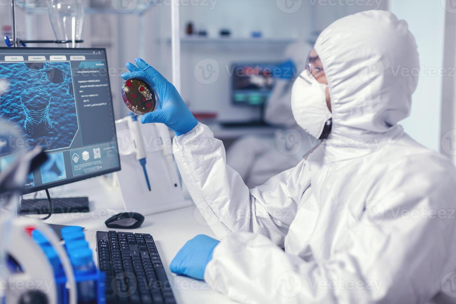 Medical scientist holding petri dish studying virus sample dressed in bacteriological suit Doctors analysing vaccine evolution using high tech researching diagnosis against covid19 virus. photo