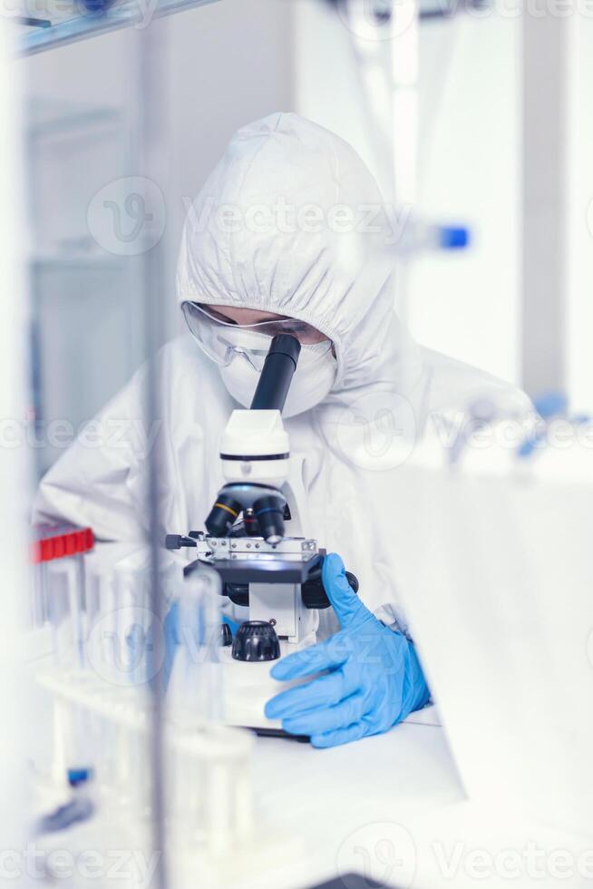 Laboratory engineer conducting experiment for vaccine against coronavirus using microscope. Chemist in coverall examining vaccine evolution using high tech researching diagnosis against covid19 virus photo